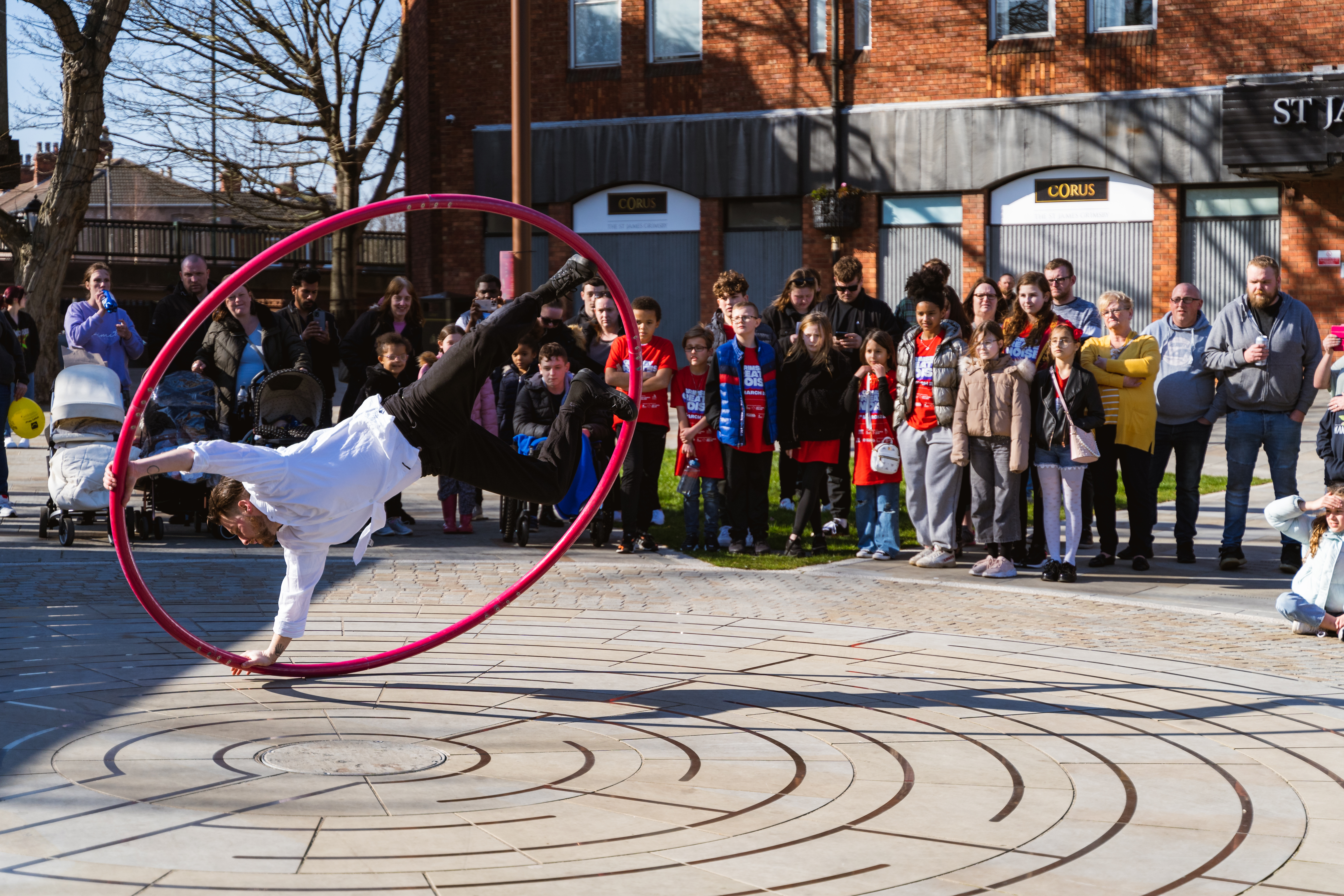 Man spinning in a large hoop with audience watching the performance in the background.