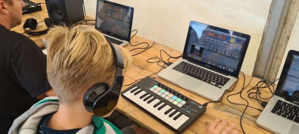 Young person wearing headphones creating digital music on a keyboard and laptop.